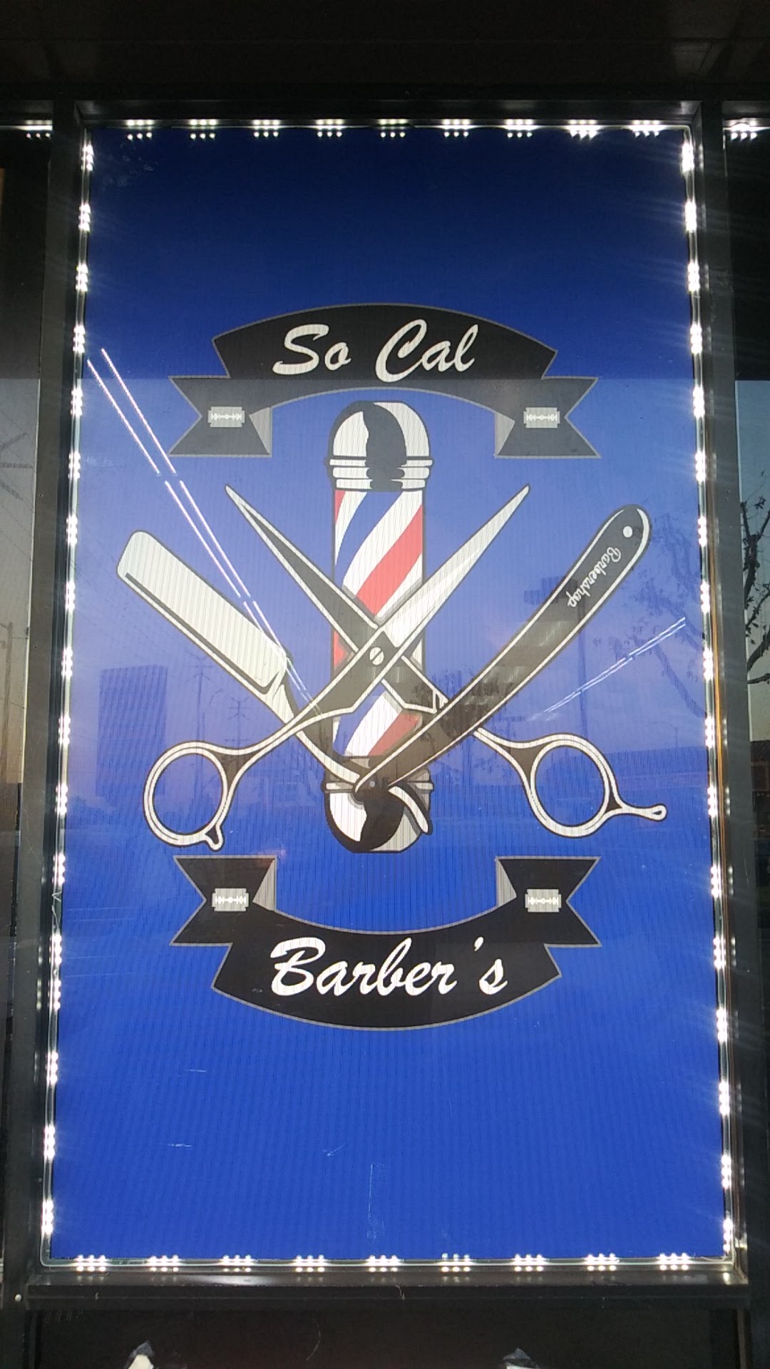 The illuminated So. Cal. Barber's sign in the shop window, showing the barber pole and crossed scissors