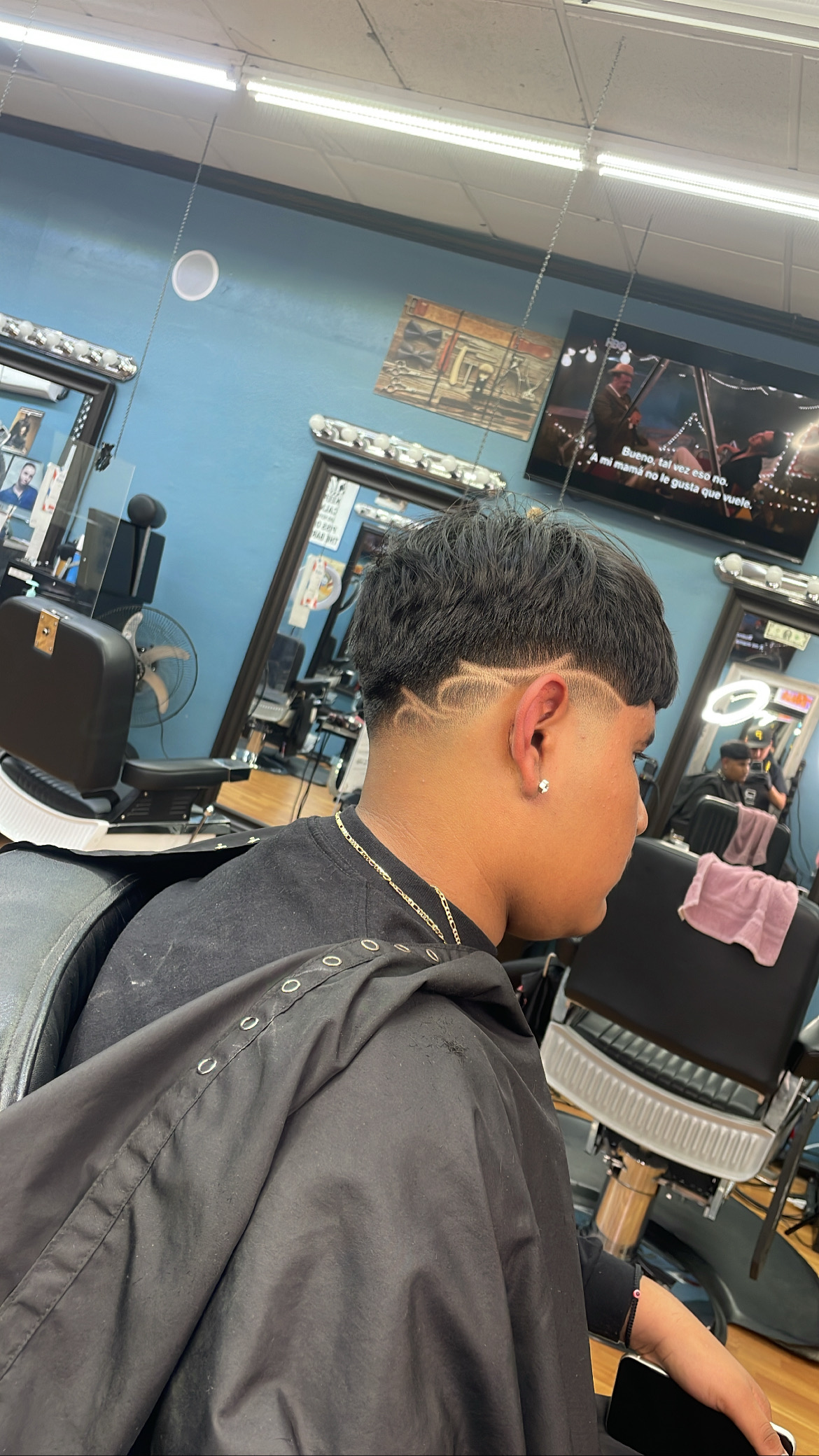 Inside So. Cal. Barber's: several stations with barber chairs and bulb-lit mirrors against blue walls